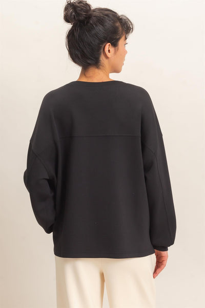 back of model wearing oversized black sweatshirt with white pants before a light background