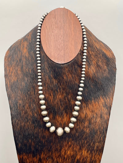 Silver beaded necklace on a wooden mannequin bust against a white background