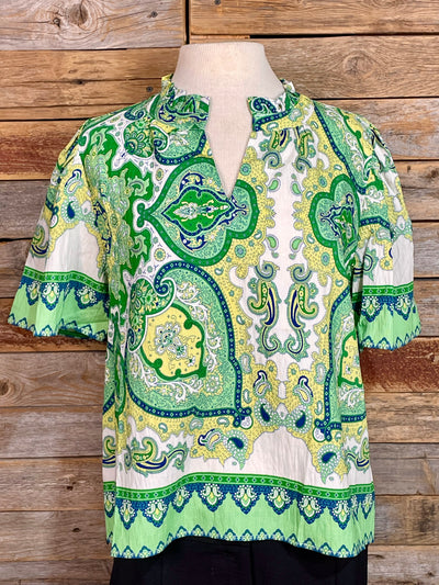 Green and blue patterned blouse on a mannequin against a wooden background