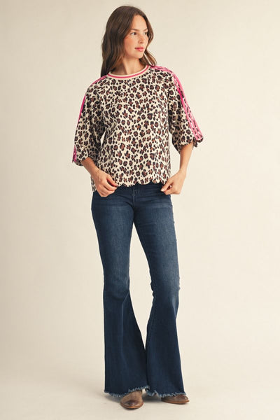 A woman wearing a leopard print top with bright pink shoulder straps and blue jeans, photographed against a plain light beige studio background.