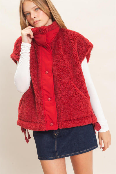 model wearing white shirt and jeans skirt with a red Sherpa Vest over it.