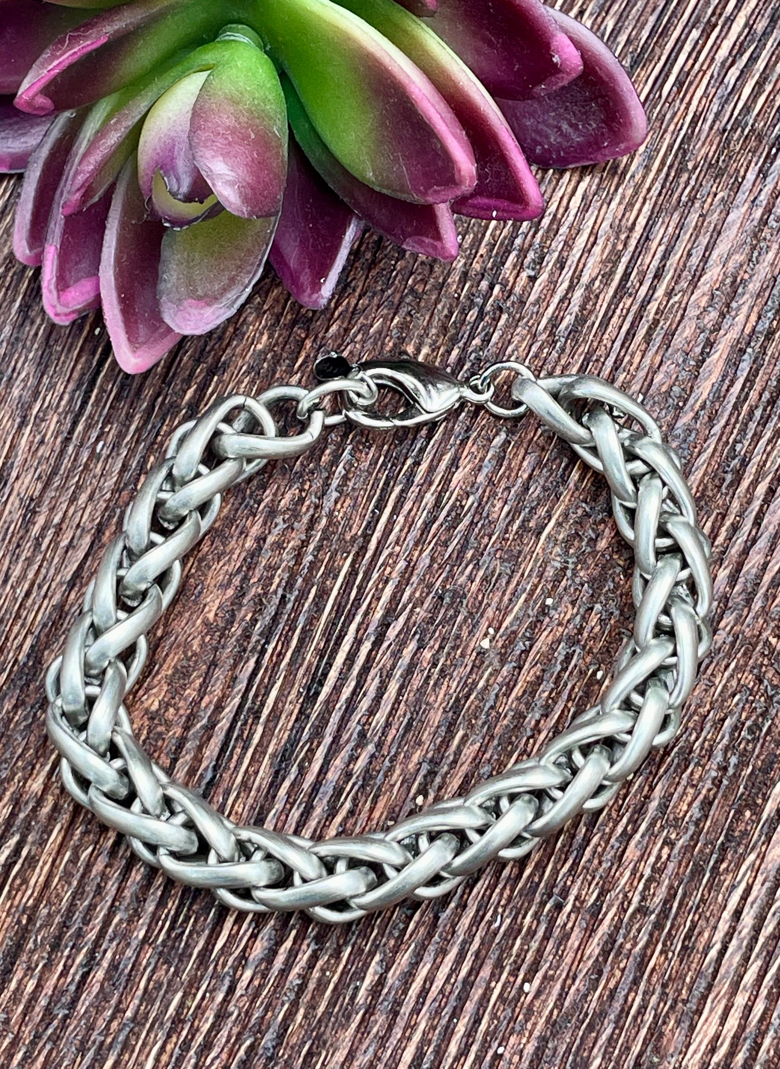 Silver braided bracelet on a wooden surface with a succulent plant.