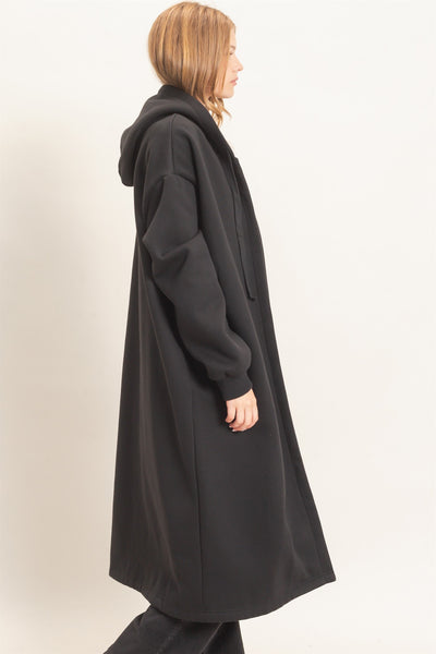 side view of model wearing a long black coat with a hood