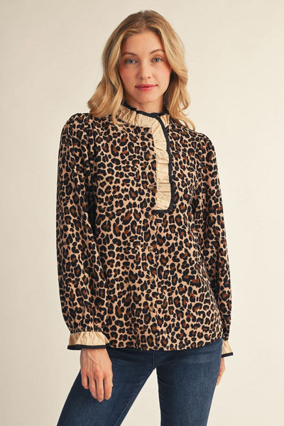 A woman modeling a leopard-print long-sleeve blouse with beige ruffle trim at the collar and cuffs, paired with blue jeans, against a plain beige studio background.