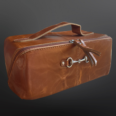 Brown leather toiletry bag with a silver buckle on a dark background