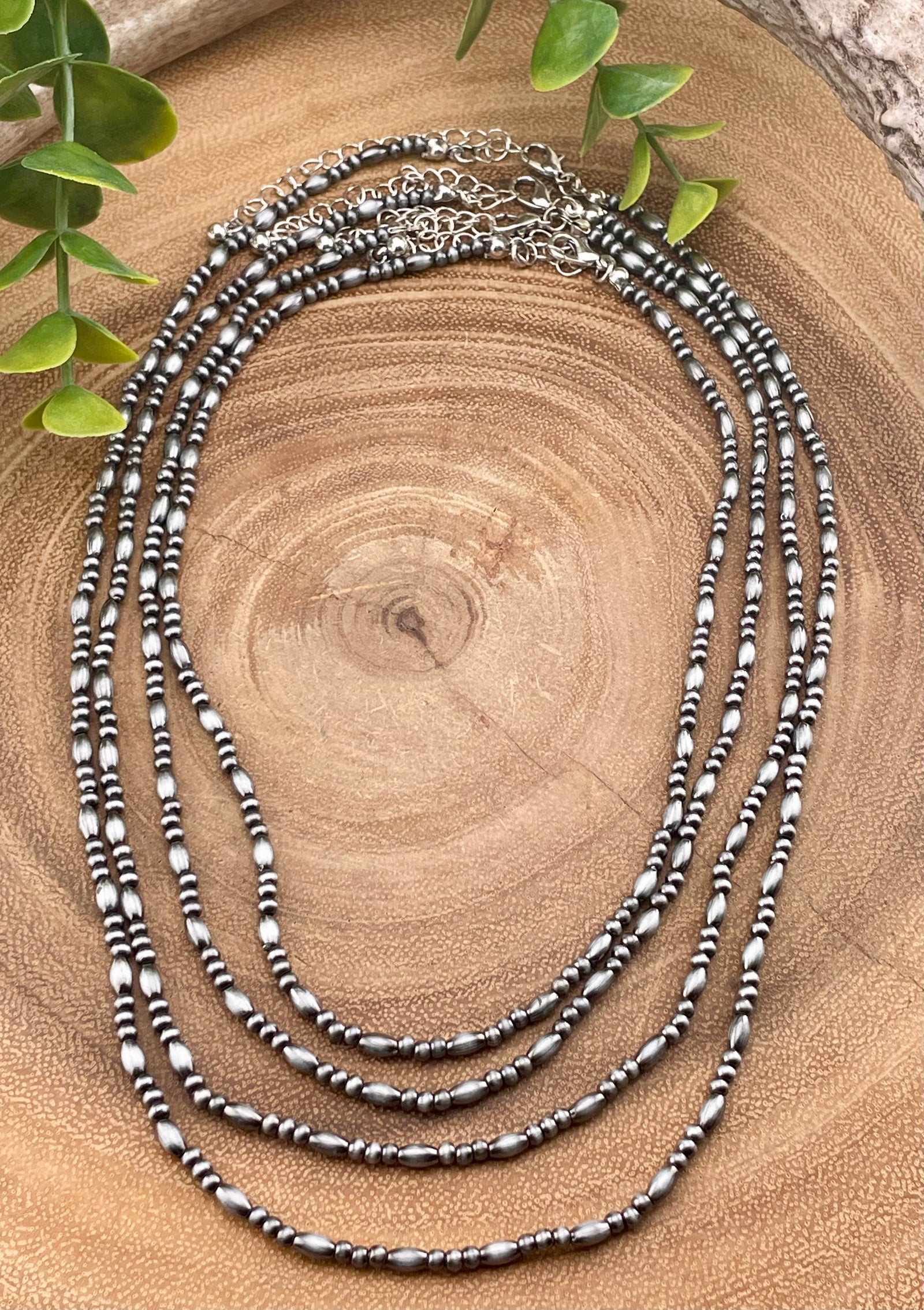 Four strand set of layered beaded necklaces on a wooden surface with green leaves.