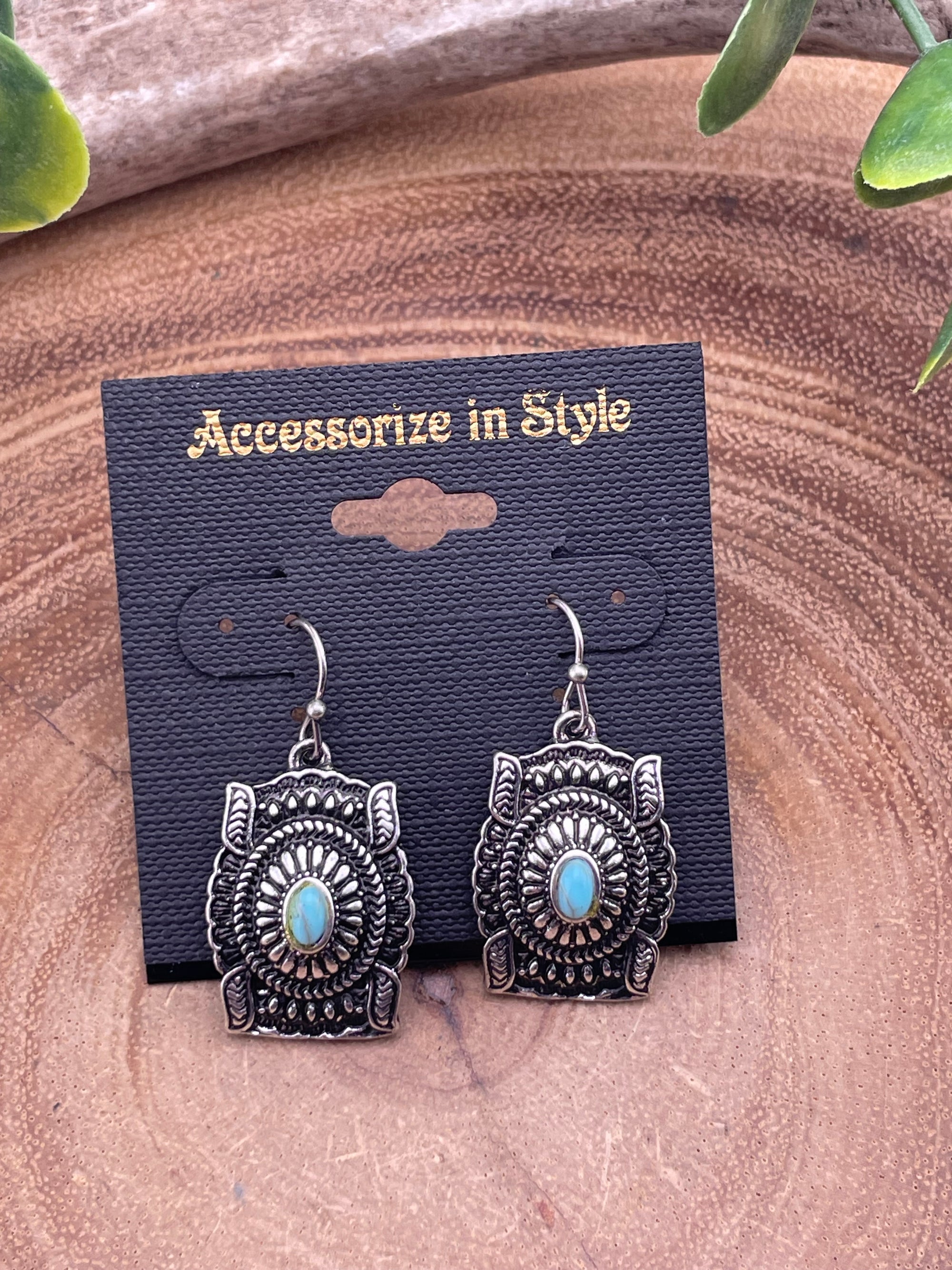 Silver earrings with turquoise stones on a black card labeled 'Accesorize in Style' against a wooden background.