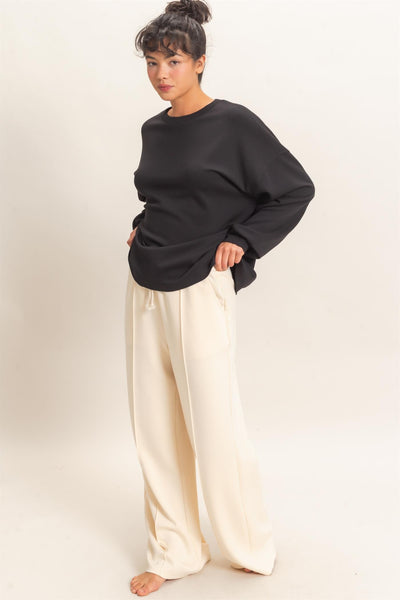 model wearing oversized black sweatshirt with white pants before a light background