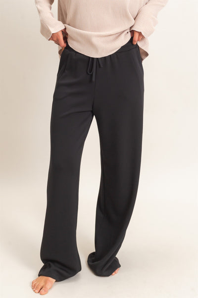 model wearing a tan shirt & black pants with a light background