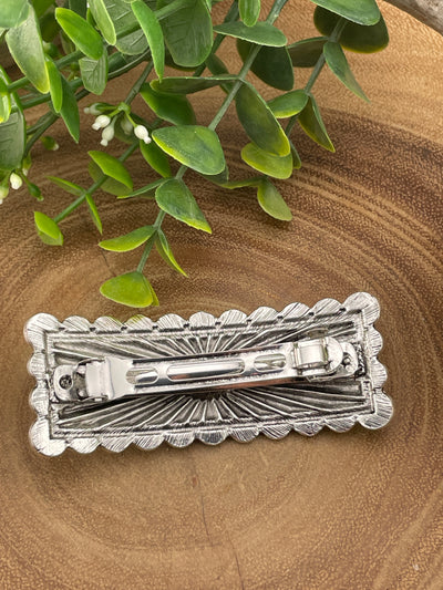 Silver hair clip on a wooden surface with green leaves