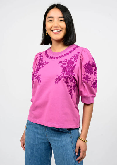 Woman wearing a pink blouse with floral embroidery on a white background