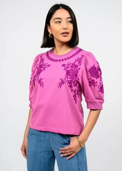 Woman wearing a pink blouse with floral embroidery on a white background