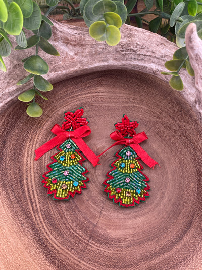 Red & Green Christmas Tree earrings with red bows on a wooden surface with greenery around.