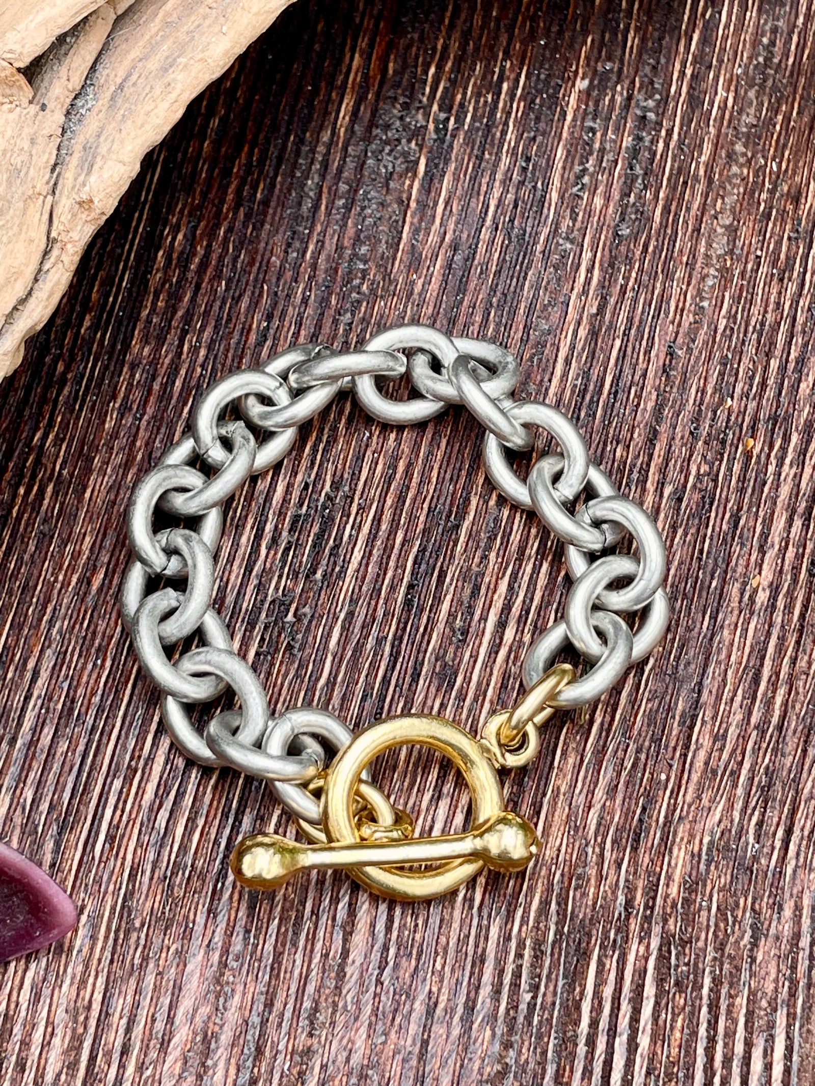 Silver chain bracelet with a gold clasp on a wooden surface