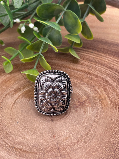 Silver floral ring on a wooden surface with green leaves.