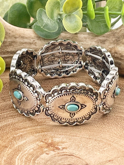fashion concho stretch bracelet with turquoise accents on a wooden background with greenery