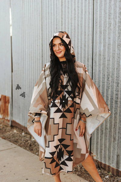Woman wearing a patterned poncho in front of a corrugated metal wall.