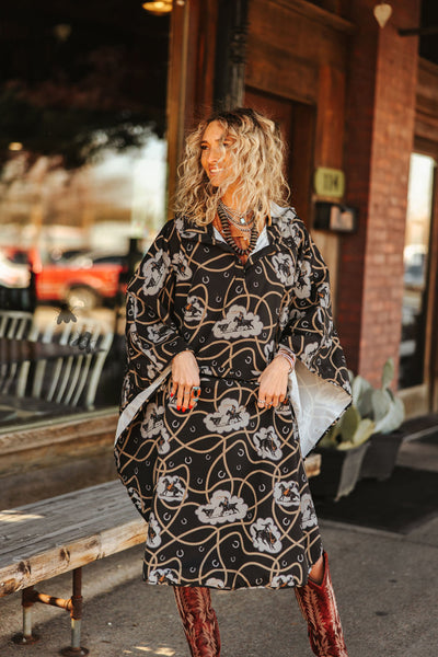 Woman wearing a black floral dress with brown boots standing on a street.