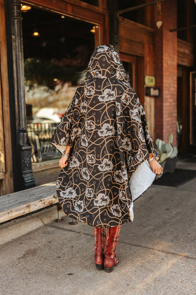 Person wearing a patterned dress and red boots standing on a sidewalk.