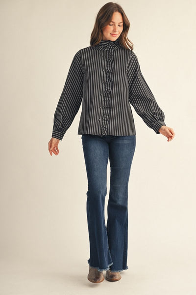 model wearing a ruffled black & white striped blouse with jeans and boots in front of a beige background