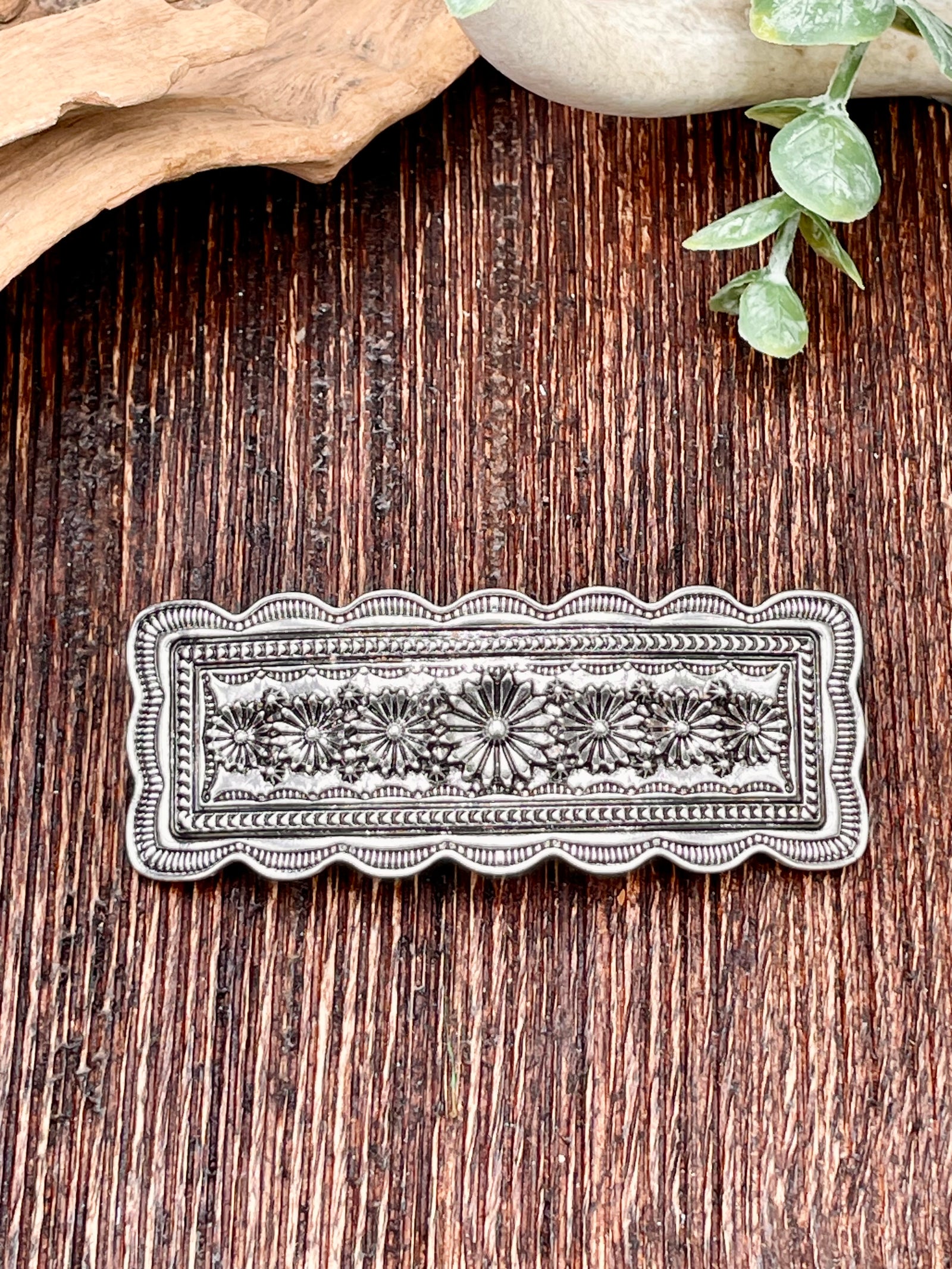 Decorative metal hair clip on a wooden surface with natural elements.
