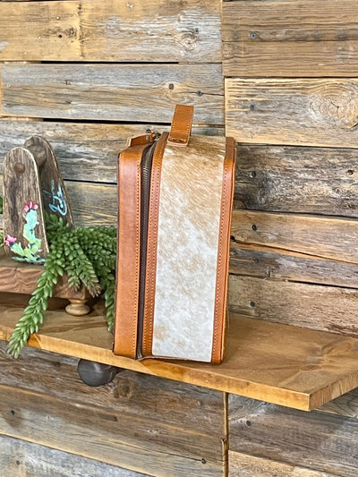 Brown leather bag with cowhide on a wooden shelf against a rustic wooden wall.