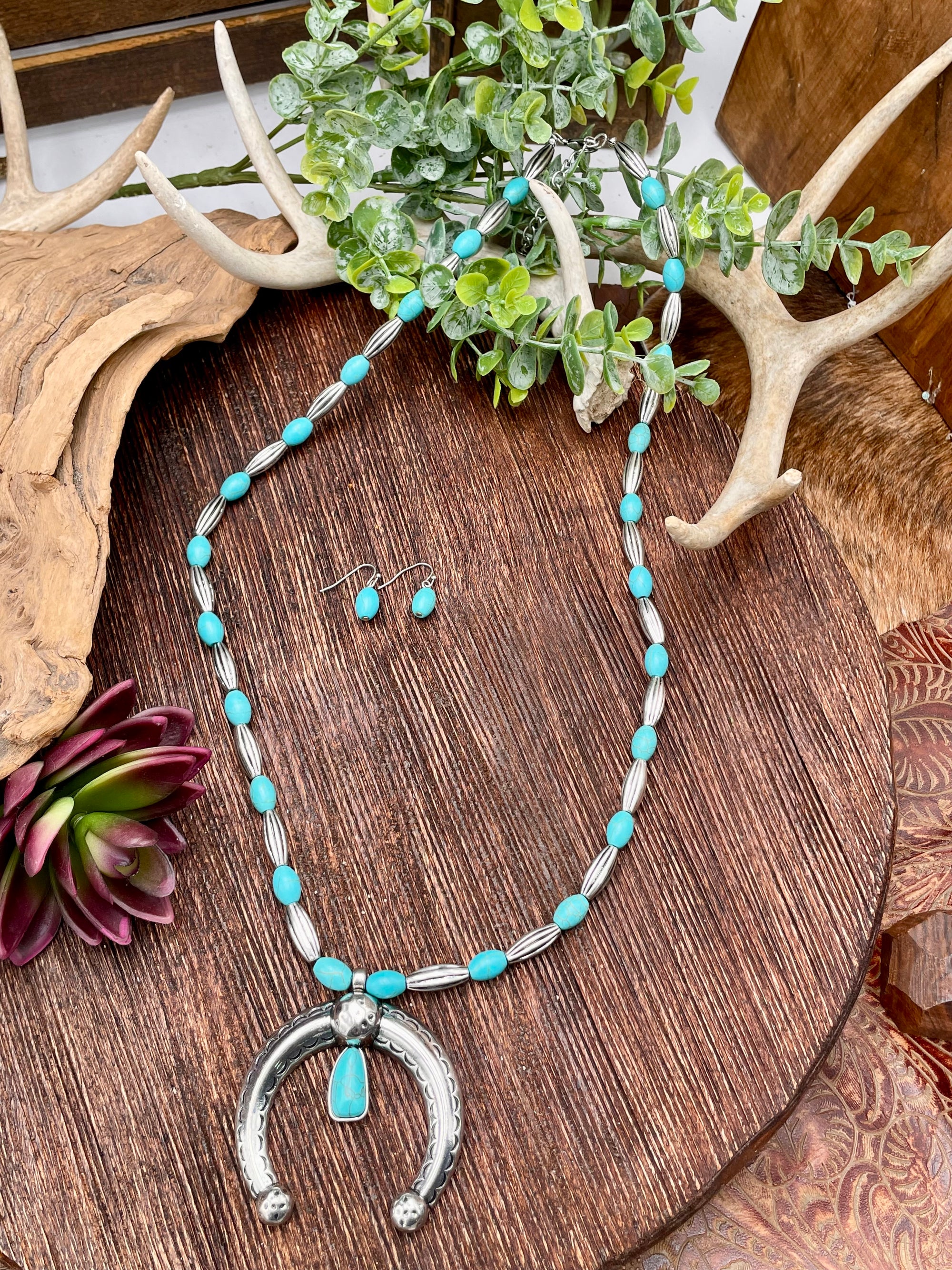 Turquoise beaded necklace and earrings on a wooden surface with antlers and plants.