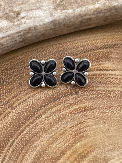 Pair of black flower-shaped earrings on a textured brown surface