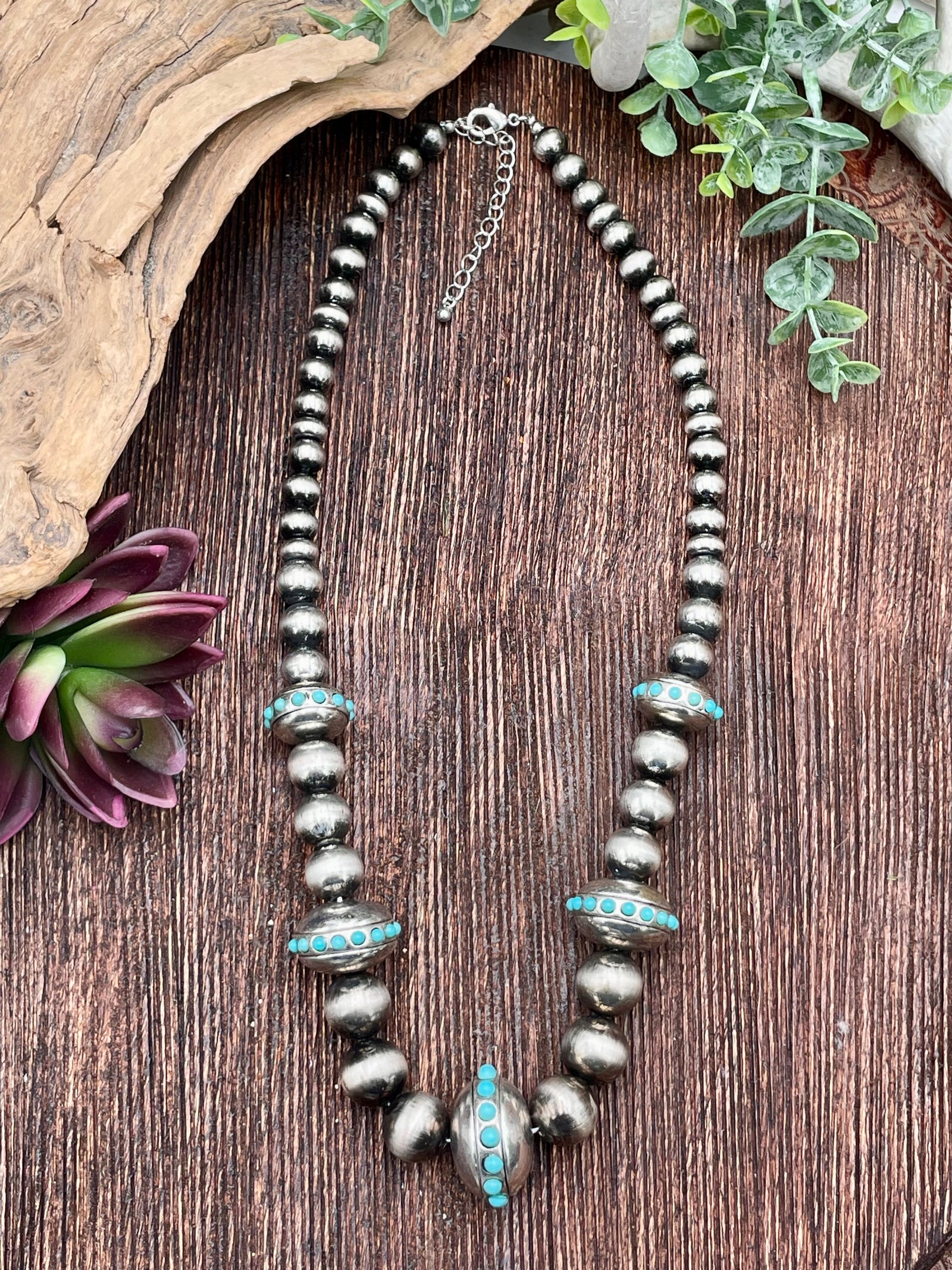 Necklace with beads and turquoise accents on a wooden surface with plants.