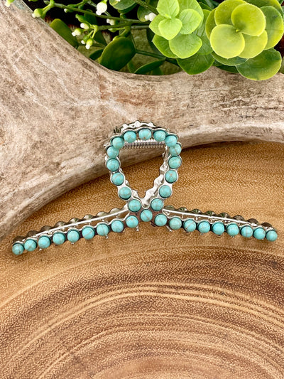 Turquoise beaded hair clip on a wooden surface with green foliage in the background