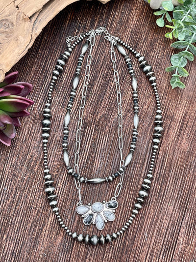 Layered beaded necklace with a black & white pendant on a wooden surface.