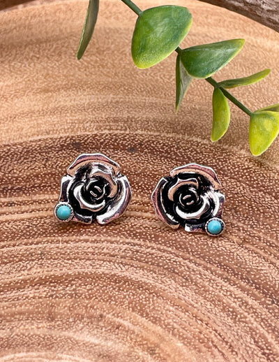 Silver rose-shaped earrings with turquoise stones on a wooden surface.