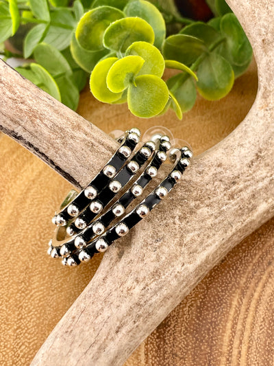Stack of silver rings on a wooden surface with green leaves in the background