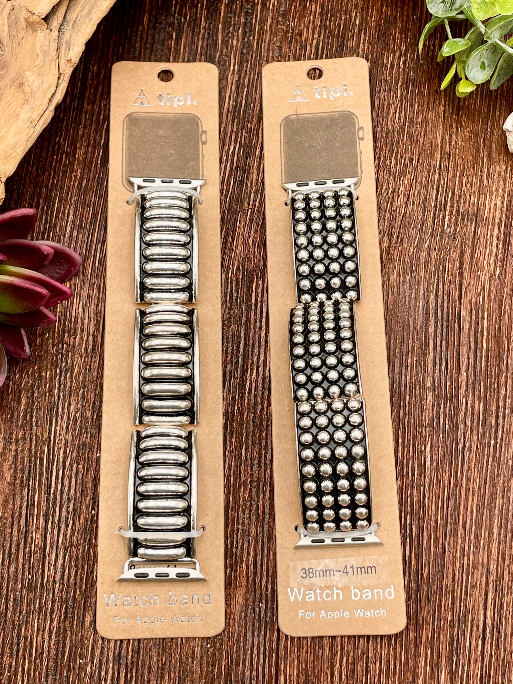 Two watch bands on a wooden surface with plants in the background