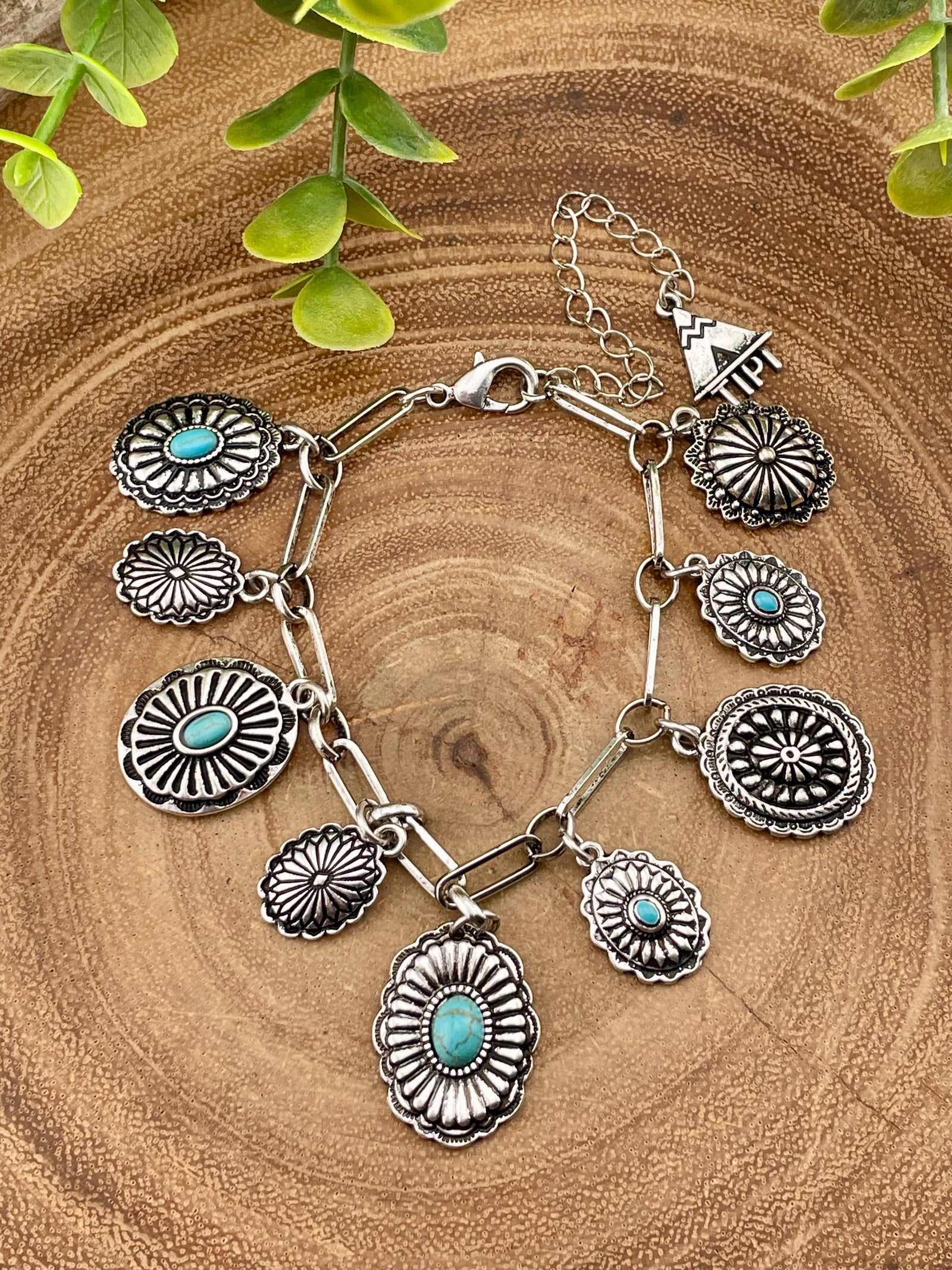 Silver concho charm bracelet with turquoise stones on a wooden surface