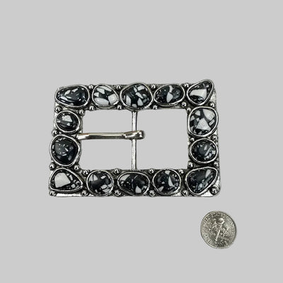 Decorative belt buckle with black stones on a tiled surface