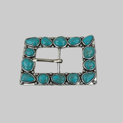 Turquoise stone belt buckle on a marble background with a coin for scale.
