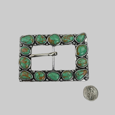 Turquoise stone belt buckle on a tiled background with a coin for scale.