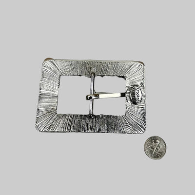 Metallic belt buckle on a textured surface with a coin for scale