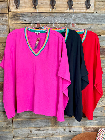 Three colorful tops hanging on a wooden wall with hooks.