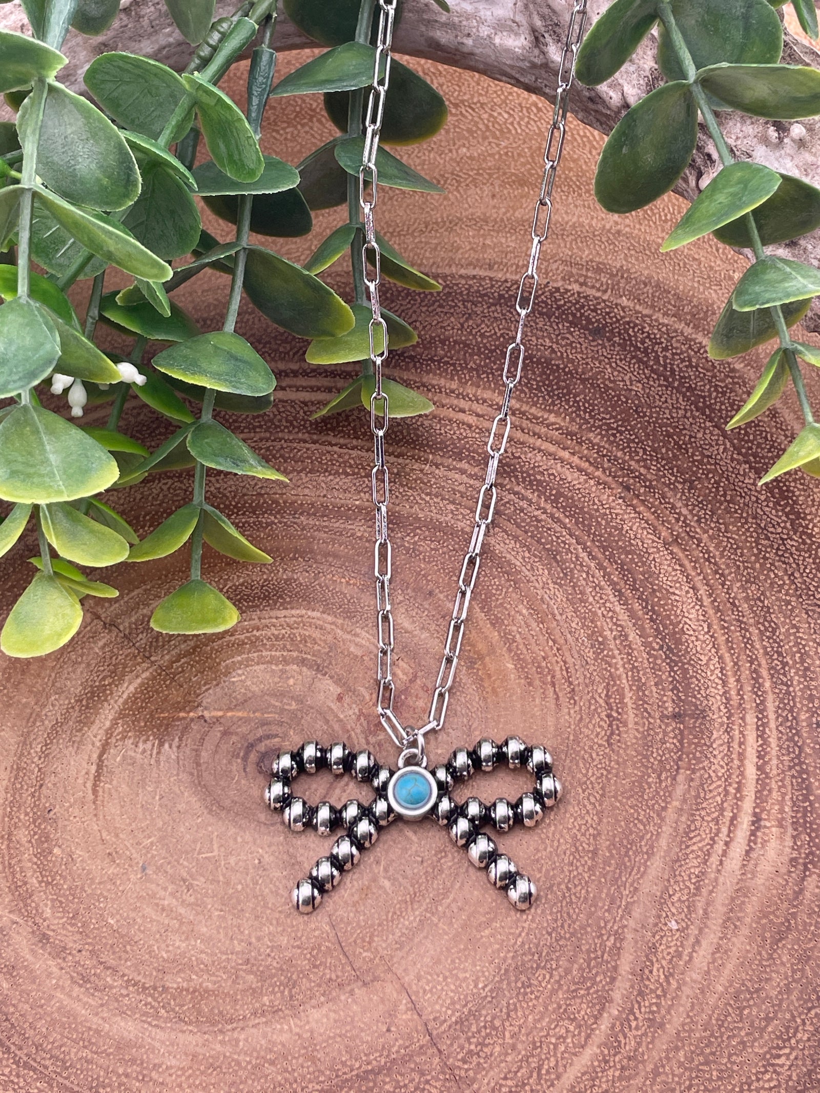 silver bead bow necklace with turquoise center stone on wooden surface