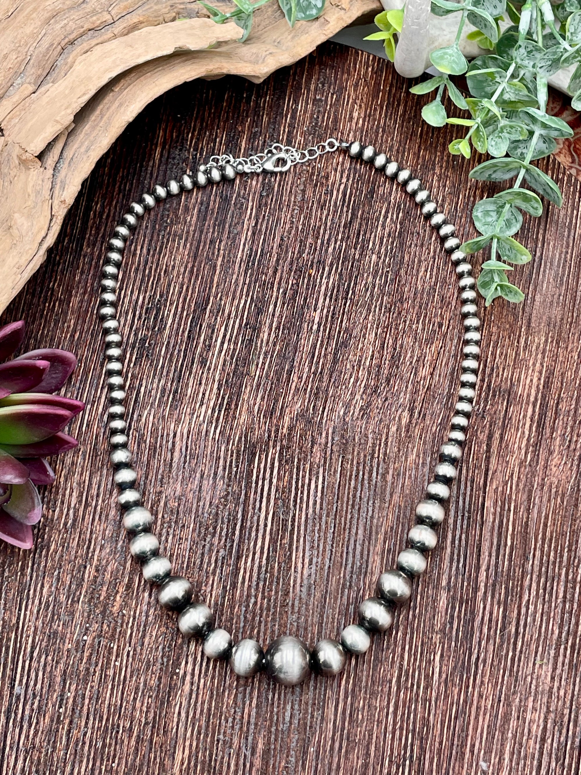 Necklace with silver beads on a wooden surface with plants.