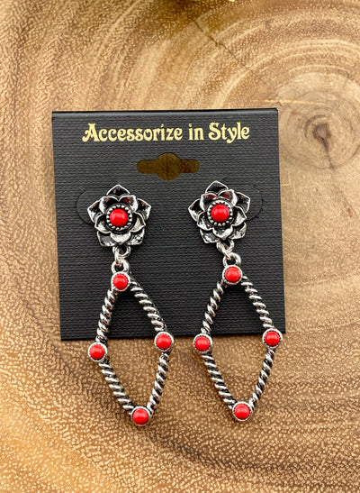 Silver floral earrings with red stones on a 'Accessorize in Style' card against a textured brown background.