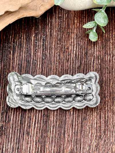 Silver hair clip with decorative design on a wooden surface