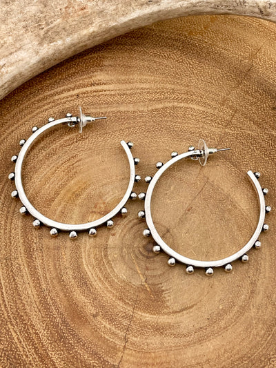 Silver hoop earrings with bead detailing on a wooden surface