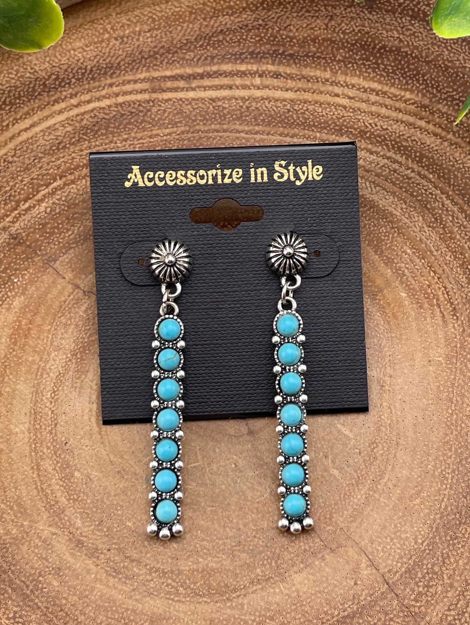 Turquoise and silver earrings on a 'Accessorize in Style' card against a wooden background