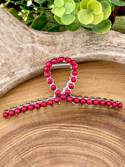 Pink beaded hair clip on a wooden surface with greenery in the background