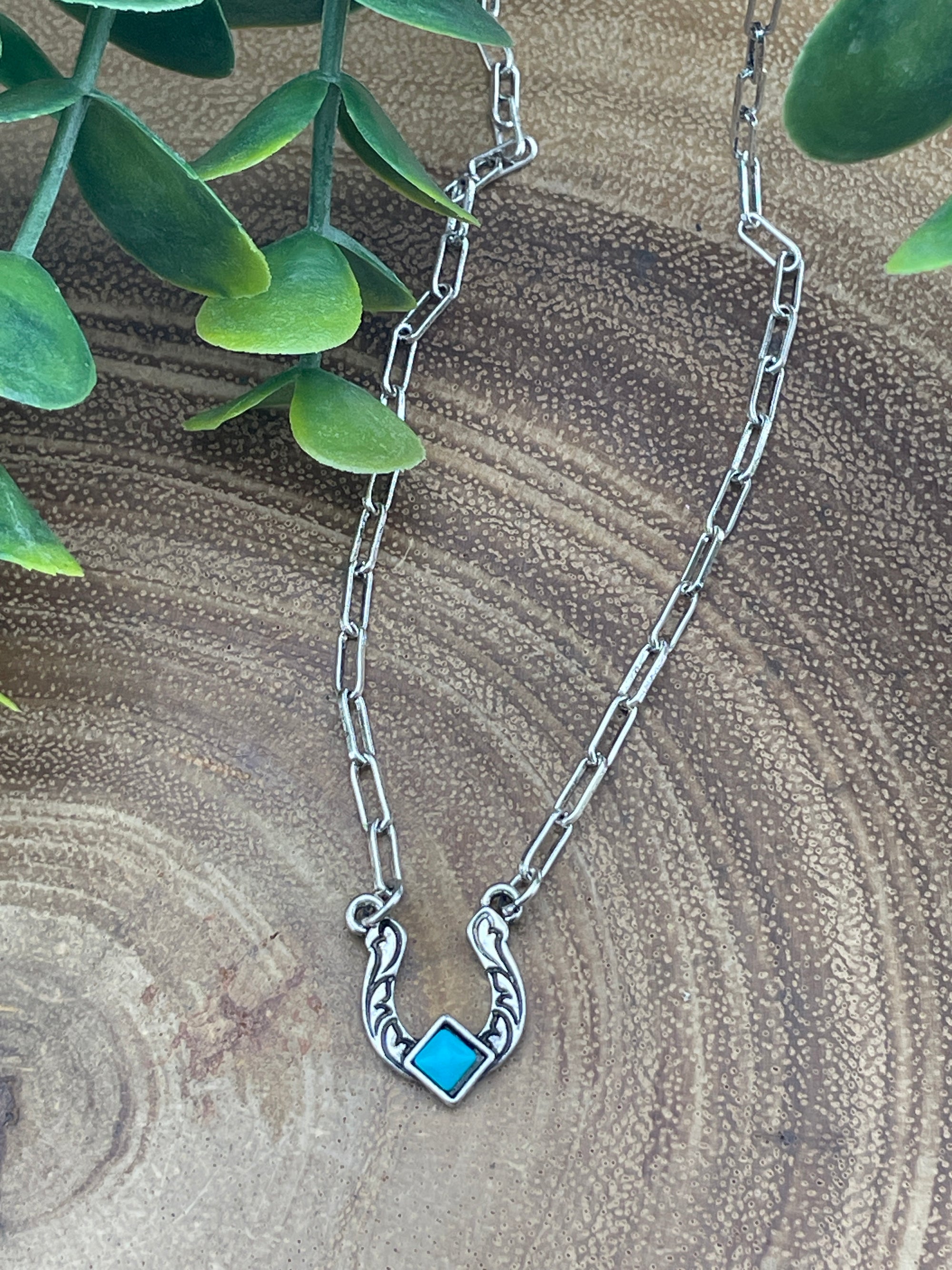 silver and turquoise horseshoe necklace on a wooden surface
