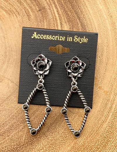 Pair of silver floral earrings with black stones on a 'Accessorize in Style' card against a beige background