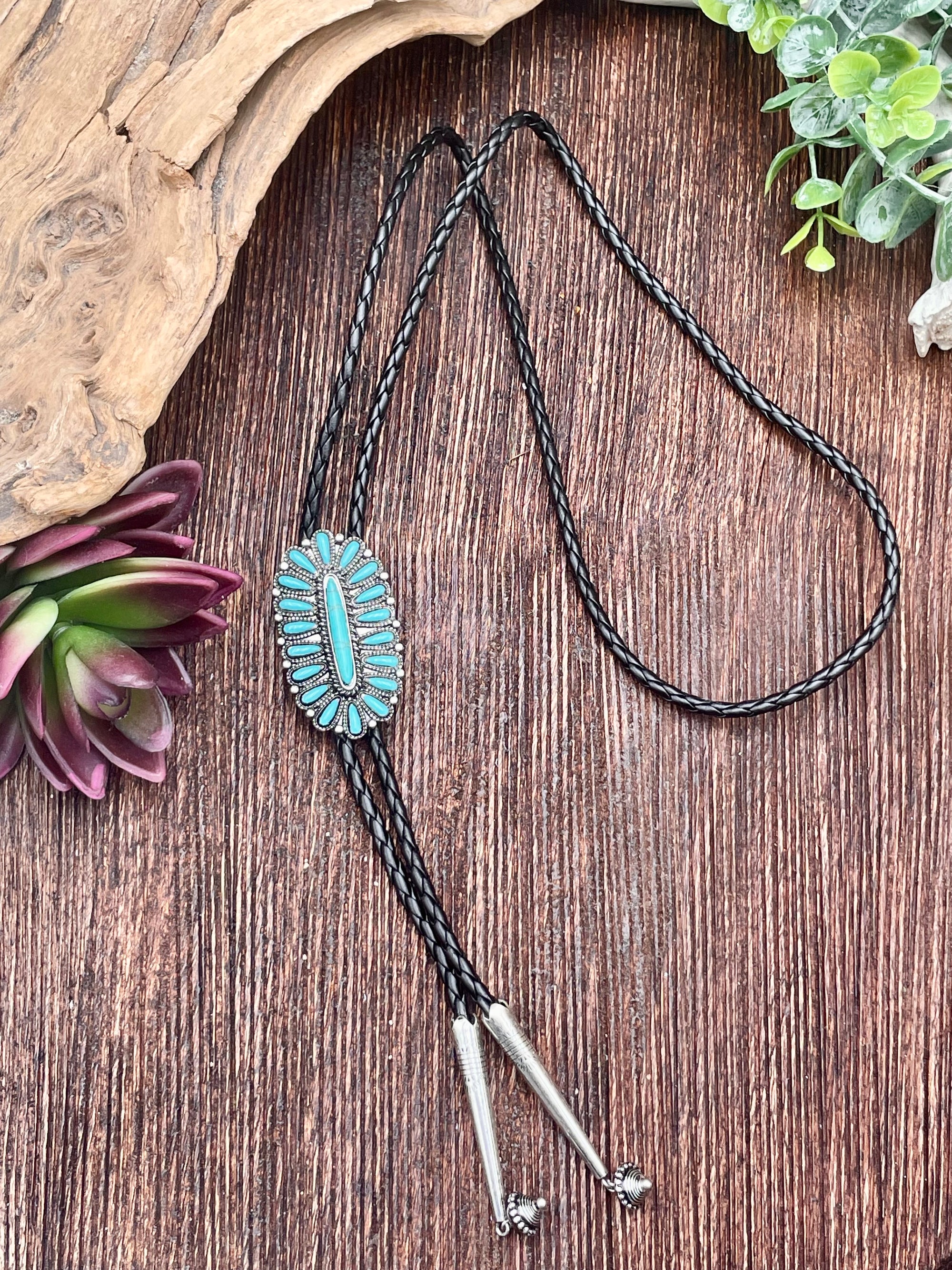 Bolo tie with turquoise stone on a wooden surface with plants